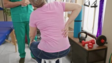 Bir erkek terapist, bir kadın hastayı fizik tedavi kliniğinde sırt egzersizleri hakkında eğitir..