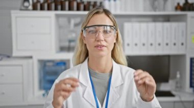 Sarışın kadın bilim adamı beyaz bir laboratuarda gözlük takıyor.