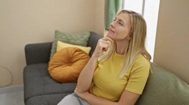 Neşeli genç bir sarışın, tişört giymiş, sevinçle 'bir numara' selamı veriyor. Evinin tam kalbinde bir aydınlanma anı. Başarı, mutluluk ve zekice bir fikir.!