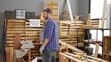 İyi donanımlı bir marangozluk atölyesinde çalışan yakışıklı sakallı adam, ahşap tahtalar ve diy aletleriyle çevrili..