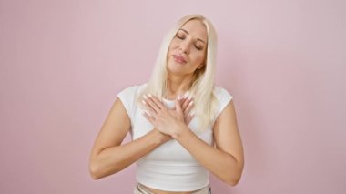 Yürekten sağlık yemini, genç, çekici sarışın kadın, gururlu ve kendine güveni tam pembe arka planda, elleri göğsünde, minnetle gülümsüyor..