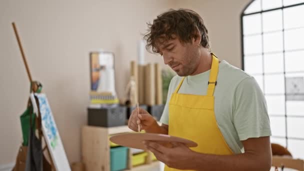 在明亮的艺术工作室里 一个戴着黄色围裙的满脸笑容的男人拿着画笔和调色板 — 图库视频影像
