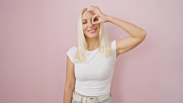 孤立したピンクの壁に立っている陽気な若い金髪の女性は カメラのために笑顔で サイン手のジェスチャーを通して承認の外観を提供しています — ストック動画
