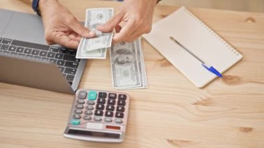 Tahta bir masadaki bilgisayar ve hesap makinesinin yanında dolar sayan bir kişi, işletme mali yönetimini ima ediyor..