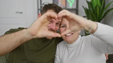 Gülümseyen bir kadın ve erkek, elleri kapalı bir yerde kalp şekli oluşturuyorlar. Rahat bir yuvada, aşkı ve birlikteliği simgeliyorlar..