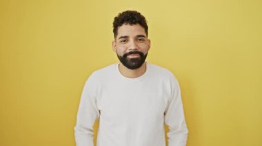 Neşeli genç bir adam, yüzünde kendine güvenen bir gülümseme, ayakta, düşüncelere dalmış, gözleri kayıp. İzole edilmiş sarı arka planda şık bir süveter giymek, yan görünüş, pozitif enerji yaymak..