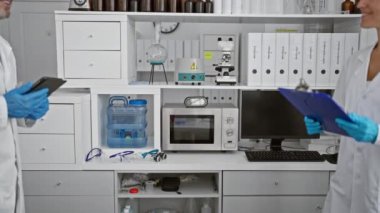 Laboratuvardaki iki memnun bilimadamı, bir dokunmatik dokunmatik yastıkta önemli bir belgeyi okurken, yoğun bir tıbbi araştırma oturumundan sonra sıcak bir anlaşma tokalaşması yaşadılar..