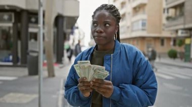 Örgülü Afrikalı bir kadın şehir caddesinde dirhem tutuyor..
