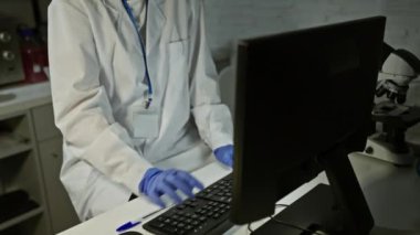 Laboratuvar önlüklü, odaklanmış genç kadın bilim adamı geceleri bilgisayar üzerinde çalışıyor..