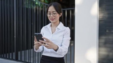 Asyalı iş kadını şehir caddesinde akıllı telefon kullanıyor.