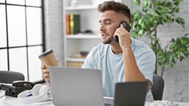 Kapalı bir ofiste elinde kahve fincanı tutarken telefonla konuşan sakallı, genç bir İspanyol..