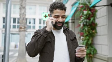 Şehir caddesinde kredi kartı tutarken cep telefonuyla konuşan yakışıklı sakallı adam..