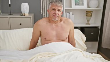 Orta yaşlı, üstsüz bir adam modern bir yatak odasında yatıp derin derin bakıyor..