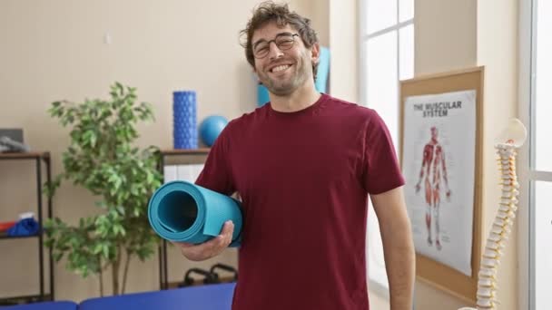 Smiling Hispanic Man Holding Yoga Mat Physical Therapy Clinic Rehabilitation — Stock Video