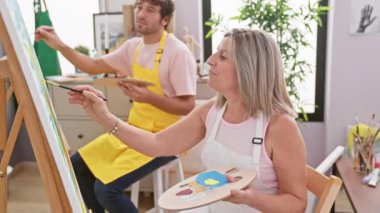 İki kendine güvenen sanatçı, erkek ve kadın, kapalı alan sanat stüdyosunda resim yaparken, birlikte resim çizmekten zevk alırlar.