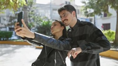 Neşeli bir çift güneşli bir şehir caddesinde selfie çekiyor, açık bir şehir ortamında sevgi ve bağlantı sergiliyorlar..