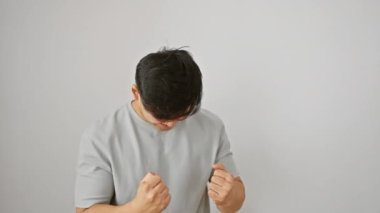 Neşeli genç Çinli adam zaferle ayakta duruyor, tişört giyiyor, heyecanlı bir şekilde çığlık atıyor beyaz bir arka planda izole edilmiş zafer jesti.