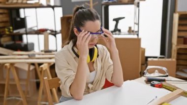 Stresli genç İspanyol kadın marangoz migrenden muzdarip. Güvenlik gözlüklü güzel bir kadın. Marangozluk atölyesinde başını ağrıtıyor.