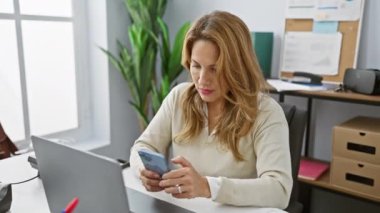 Modern ofiste akıllı telefon kullanan İspanyol iş kadını, teknolojiyle başarı ve memnuniyeti ifade ediyor.