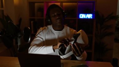 Afrikalı Amerikalı adam geceleri loş bir oyun odasında sanal gerçeklik kulaklığını inceliyor..