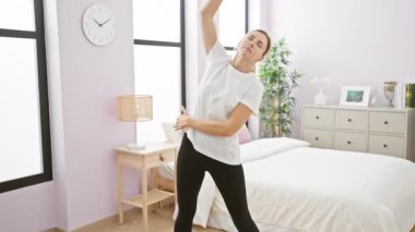 Parlak yatak odasında esneme egzersizleri yapan genç bir kadın canlılık ve sabah tazeliği yayıyor..