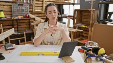 Tutkulu genç İspanyol kadın marangoz, hareketli marangozluk atölyesinde tasarımlar çizerken video çağrısına katılıyor.