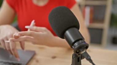Kafkas bir kadın modern bir stüdyoda podcast kaydında ellerini gösteriyor, teknoloji ve iletişimi vurguluyor..