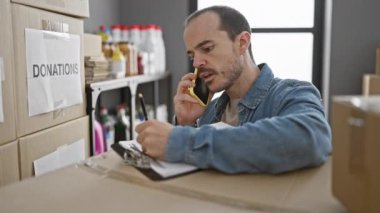 Gönüllü, sakallı bir İspanyol, telefonla konuşurken içeride bağış organize ediyor ve notlar alıyor..