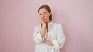 Depresyonla uğraşan yorgun ve sıkılmış genç bir kadın, kollarını çaprazlayarak ayakta duruyor, soyutlanmış pembe bir arka plana karşı sorunlarını düşünüyor.