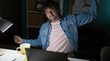 İspanyol adam geceleri ofiste kahve ve dizüstü bilgisayarın yanında yoruluyor.