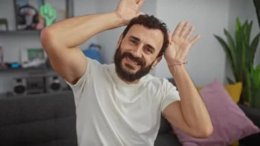 Şüpheci orta yaşlı bir adam evde tavşan kulağı yapıyor, beyaz bir tişört giyiyor, Paskalya için alaycı bir şekilde sırıtıyor.