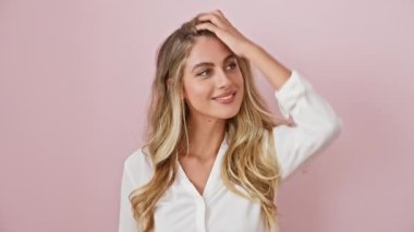 Neşeli genç sarışın kadın, kendine güvenen ve modaya uyan, tebessüm ve el teması ile poz veren, izole edilmiş pembe arka planda duran, çekici bir gömlek giyen..