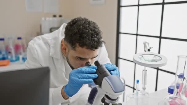 Joven Hispano Con Barba Trabaja Laboratorio Usando Microscopio Retratando Entorno — Vídeo de stock