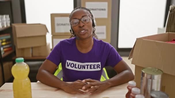 身穿印有 志愿者 字样的耳机和紫色衬衫 在仓库做义工的非洲裔美国妇女 — 图库视频影像