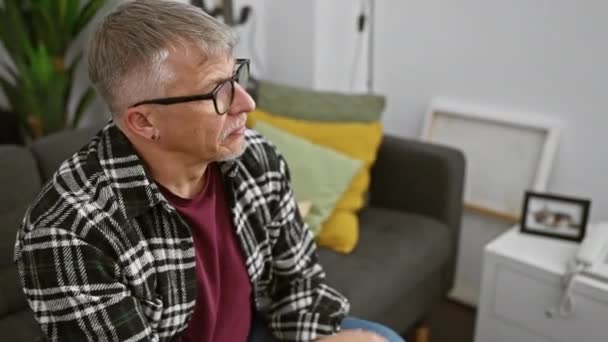 Zamyślony Starszy Mężczyzna Okularach Salonie Odzwierciedlający Swobodnym Otoczeniu Domowym — Wideo stockowe