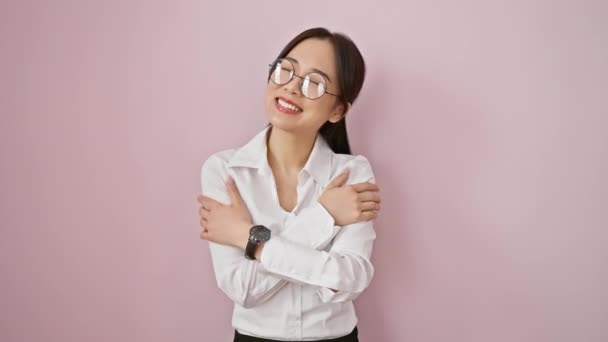 戴着眼镜的快乐的中国年轻女性以拥抱的方式表达了自己的爱意 在孤立的粉色背景下流露出自信 — 图库视频影像