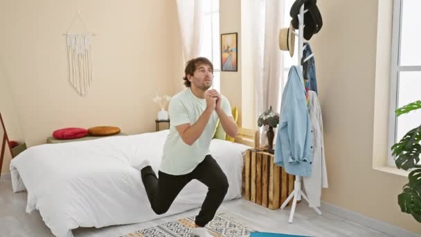 ベッドルームの敷物にひざまずいて 明るく家庭的なインテリアの中で反射的な気分を表現する若い男 — ストック動画