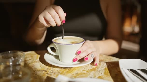 居心地の良い喫茶店のテーブルでカプチーノの新鮮なカップを味わう女性 周囲の屋内照明で照らされた — ストック動画