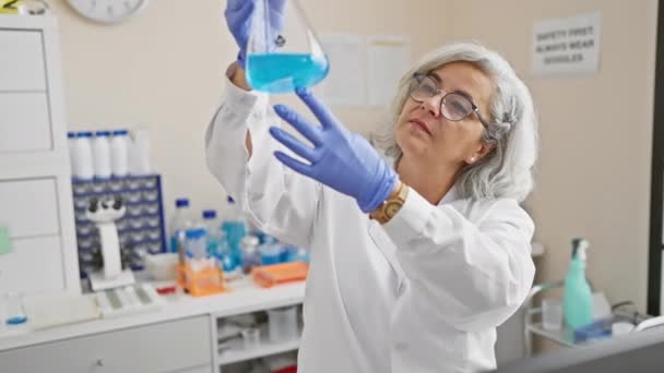 一位成熟的女科学家在实验室里检查瓶子里的蓝色化学物质 代表了专业水平和研究水平 — 图库视频影像