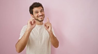 Sakallı yakışıklı genç adam pembe bir arka planda kamerayı işaret ediyor.
