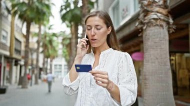 Elinde kredi kartı olan ve şehirde telefonla konuşan odaklanmış genç bir kadın.