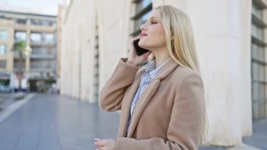 Gülümseyen yetişkin bir kadın akıllı bir telefonla konuşuyor. Şehir caddesinde yürürken, gündelik tarz ve güven yayıyor..