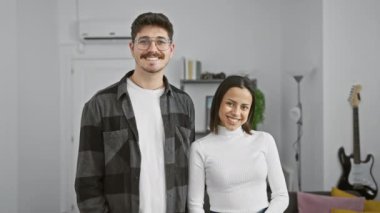 Gülümseyen bir erkek ve kadın, gitar geçmişi olan modern bir oturma odasında sevgiyle kucaklaşır.