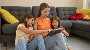 Gülümseyen bir kadın ve iki kız, rahat bir oturma odasındaki kanepede birlikte tablet kullanmaktan hoşlanırlar..