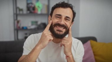 Onun rahat evinde, yakışıklı bir orta yaşlı beyefendi, neşeli bir gülümseme zorlayan beyaz bir tişört spor; parmakları işaret ederek, dudakları onun sağlıklı dişleri parlayan açık ağızlı bir sırıtış.