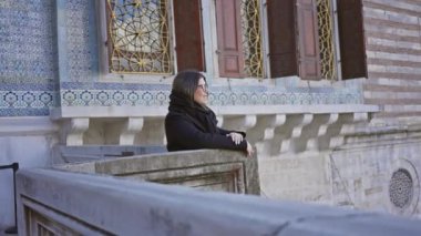 İstanbul 'daki Topkapı Sarayı' nın balkonuna yaslanmış eşarplı bir kadın geleneksel mimarisini sergiliyor..