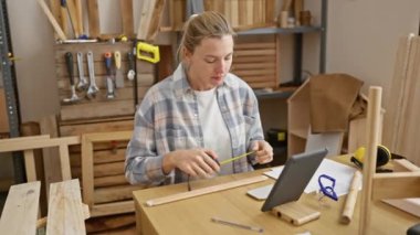 Odaklanmış bir kadın atölyede odun ölçüyor.