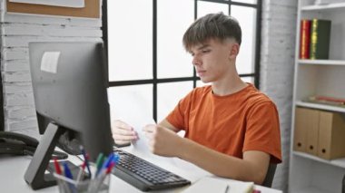 Modern üniversite kütüphanesinde bilgisayar okuyan beyaz bir çocuk.