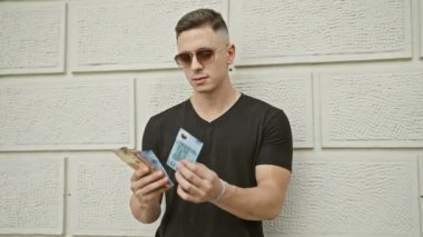 Güneş gözlüklü yakışıklı bir genç şehir sokaklarında Meksika pesoları sayıyor..