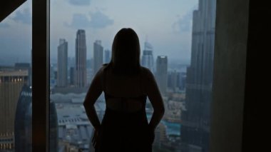 Dubai siluetini gün batımında gözlemevinden izleyen genç bir kadının arka ışıklandırılmış silueti.
